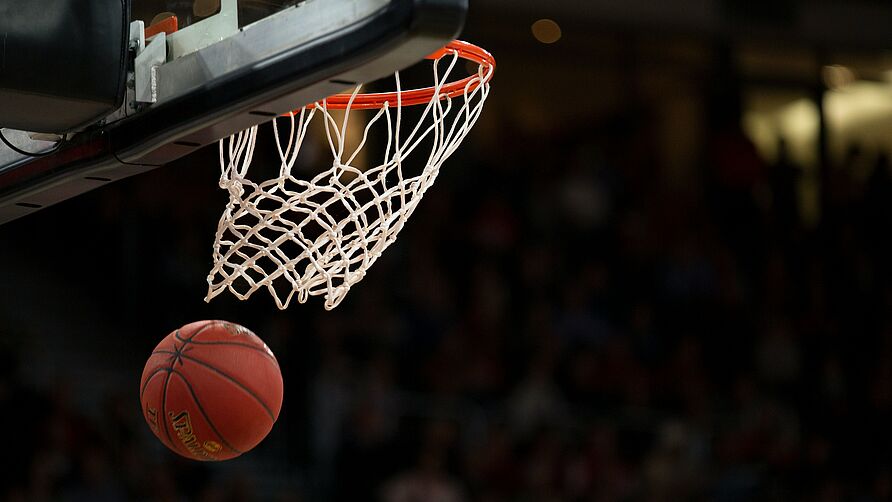 Ein Basketball, der durch das Netz des Korbes fällt.