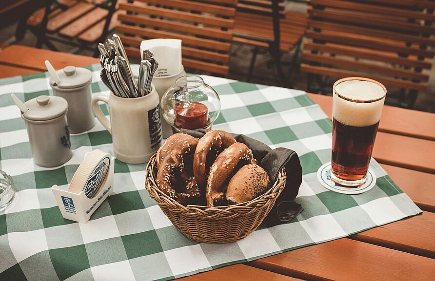 Ein gedeckter Tisch mit Tischdecke, Besteck, Brezeln und einem Bier.