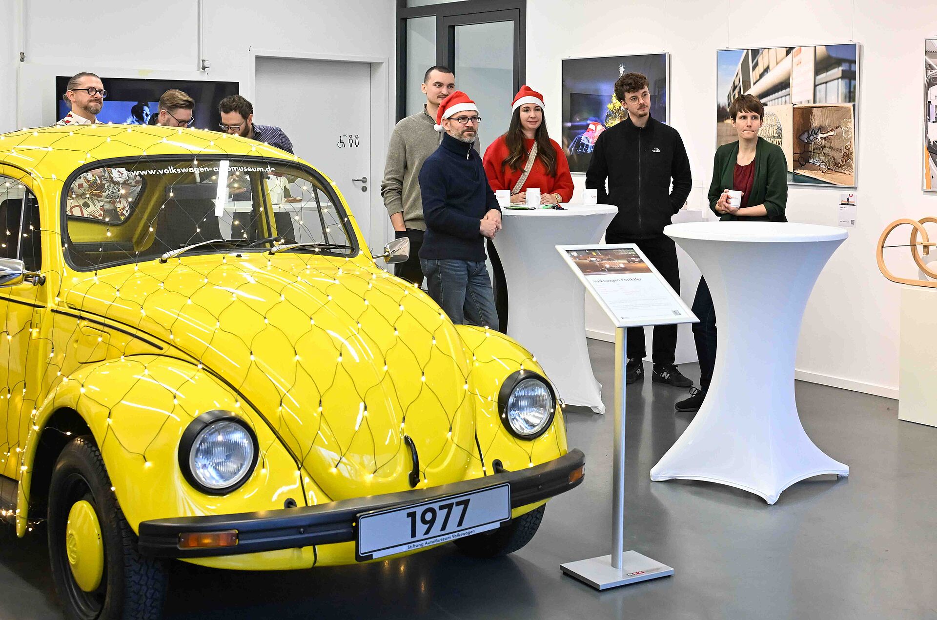 NFF-Nikolausfeier am 06. Dezember 2024: Gruppe steht im Galerieraum neben einem gelben VW-Käfer