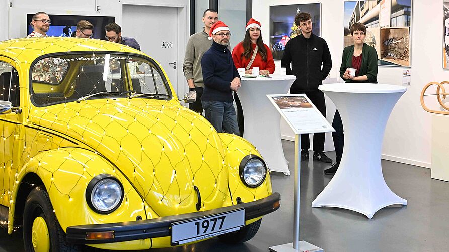 NFF-Nikolausfeier am 06. Dezember 2024: Gruppe steht im Galerieraum neben einem gelben VW-Käfer