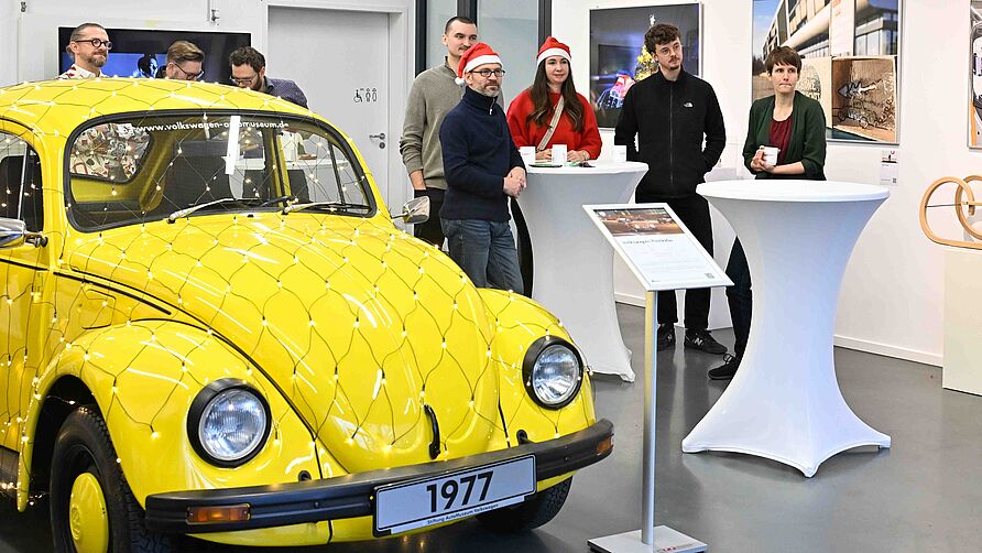 NFF-Nikolausfeier am 06. Dezember 2024: Gruppe steht im Galerieraum neben einem gelben VW-Käfer