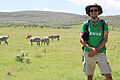 Student Nils Michalke stands in a steppe landscape. Zebras graze in the background.