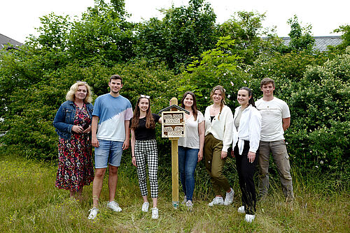 A group of students stands around an insect hotel.