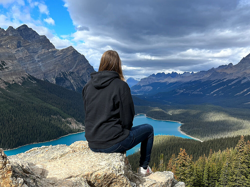 A student sits on a cliff in the Rocky Mountains with a view of the Canadian mountain landscape. 