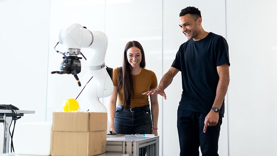 A man and a woman stand in front of a robotic arm