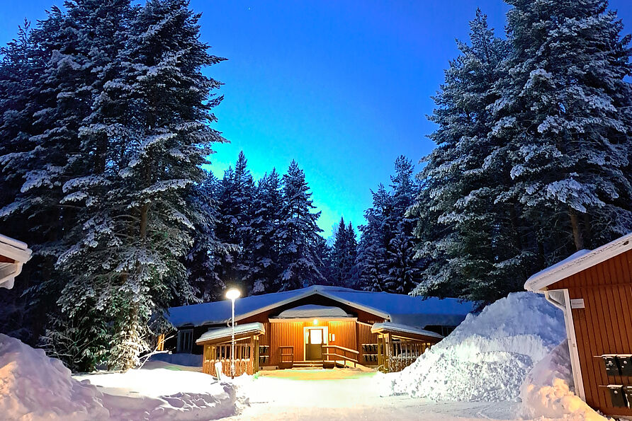 Eine beleuchtete Hütte in einem verschneiten Wald in Schweden.